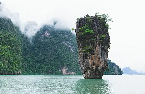 Grand piton rocheux couvert de végétation surgissant de la mer dans la brume.