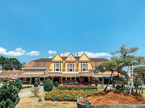 Bâtiment de style colonial avec jardin fleuri et allées sous un ciel bleu.
