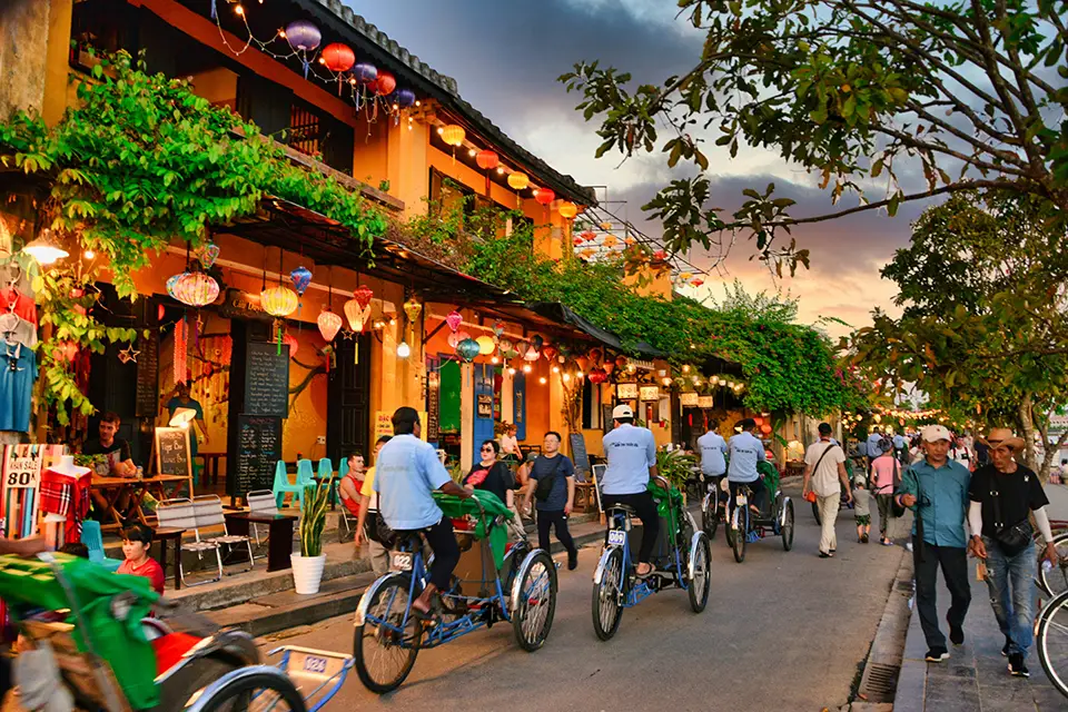 Rue animée de Hội An au crépuscule, avec lanternes colorées et cyclo-pousses, au Vietnam.