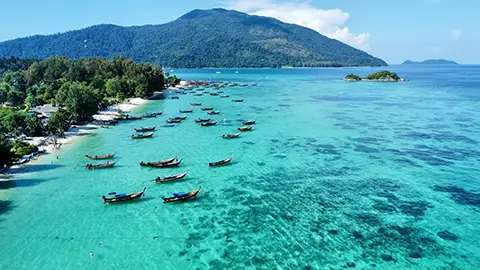 Eau turquoise vue du ciel avec de nombreux bateaux près d’une plage tropicale.