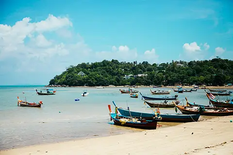 Plage de sable clair avec bateaux traditionnels amarrés dans une eau peu profonde.