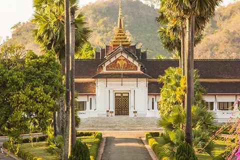 Temple entouré de palmiers avec toiture décorée et stupa doré.