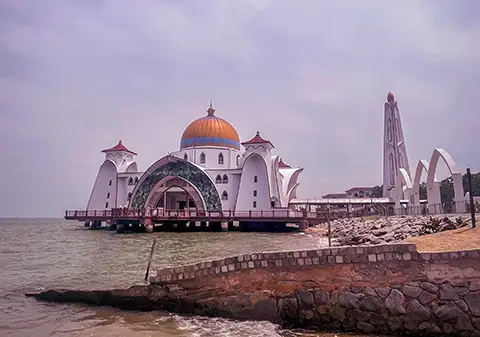 Mosquée au bord de l’eau avec dôme et minaret sous un ciel gris.
