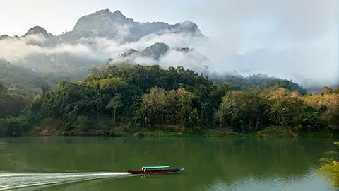 Paysage de rivière avec montagnes brumeuses et petite embarcation.