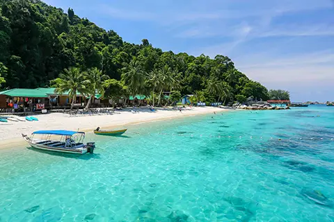 Plage tropicale avec bateaux ancrés dans une eau turquoise très claire.