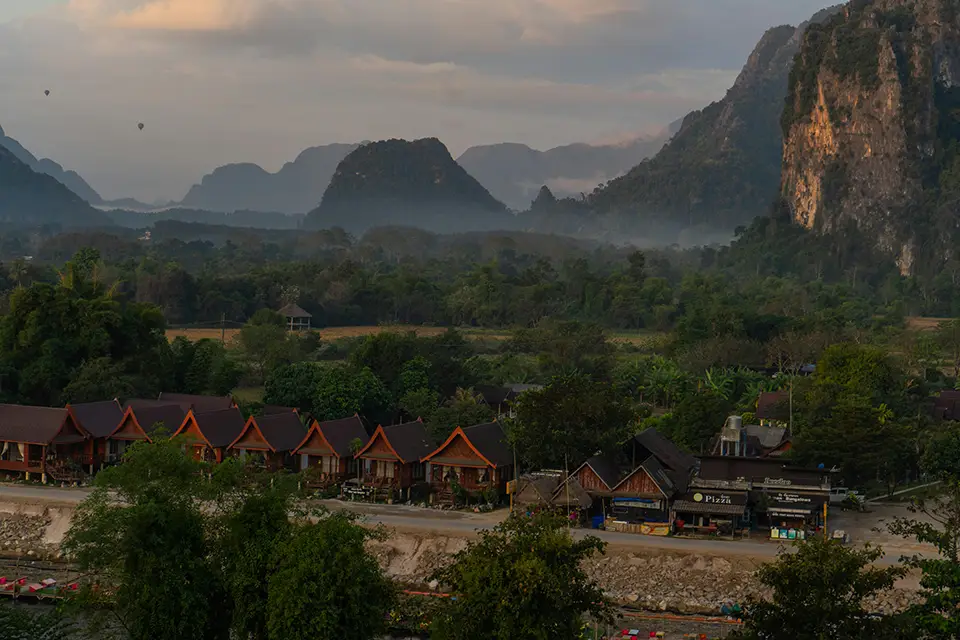 Paysage karstique de Vang Vieng au Laos, avec montagnes verdoyantes, village traditionnel et rizières au premier plan.