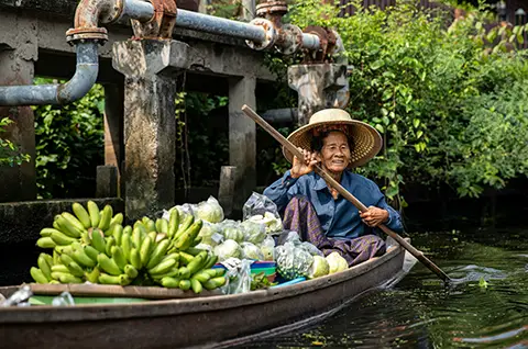 Femme au chapeau conique vendant des fruits depuis une petite barque.