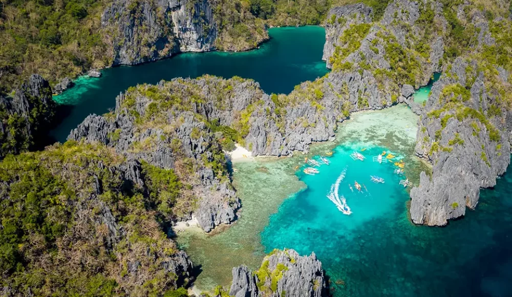 Vue aérienne d’une lagune turquoise entourée de falaises calcaires et de bateaux.