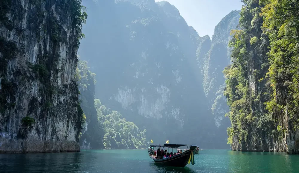 Bateau long-tail sur un lac entouré de falaises karstiques et de forêt tropicale.
